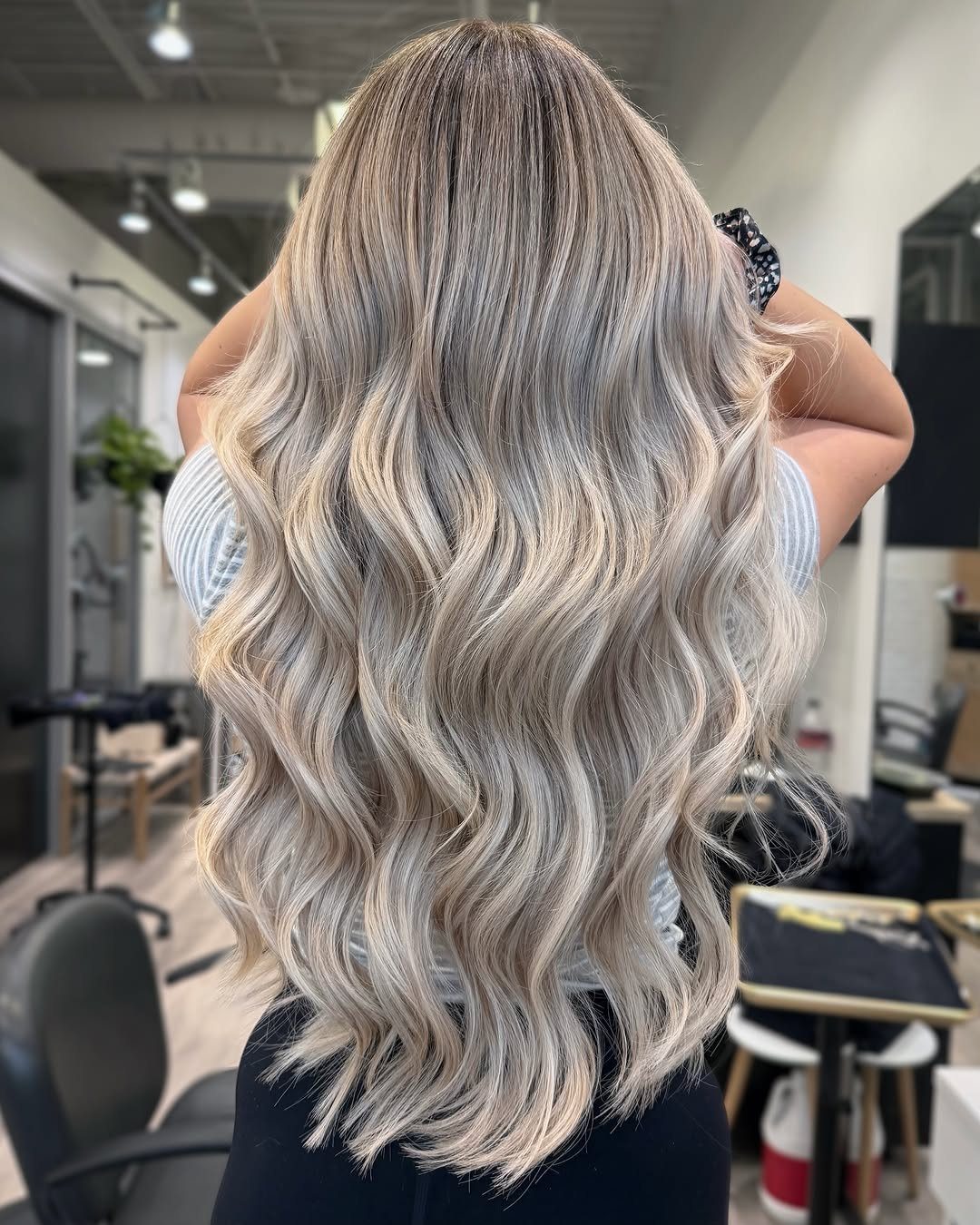 Long pearl-platinum waves with dark roots shown from behind in a salon
