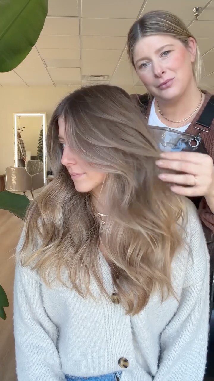 Woman with long wavy light blonde hair and dark roots in a salon