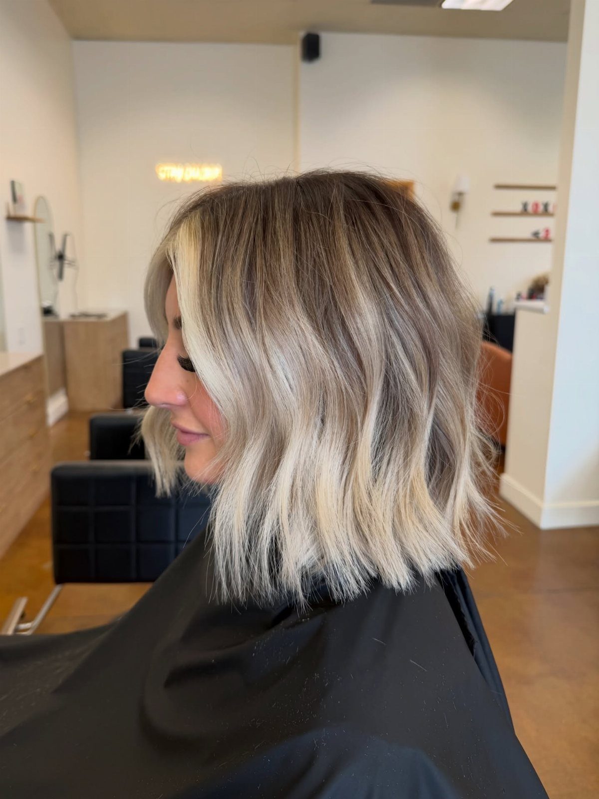 Woman showing rooted blonde bob with softly wavy pale ends in salon