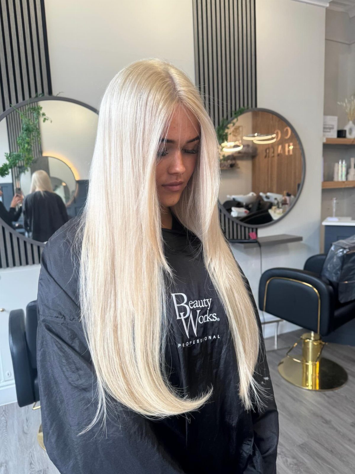 Waist-length icy blonde extensions fall straight over a black salon cape