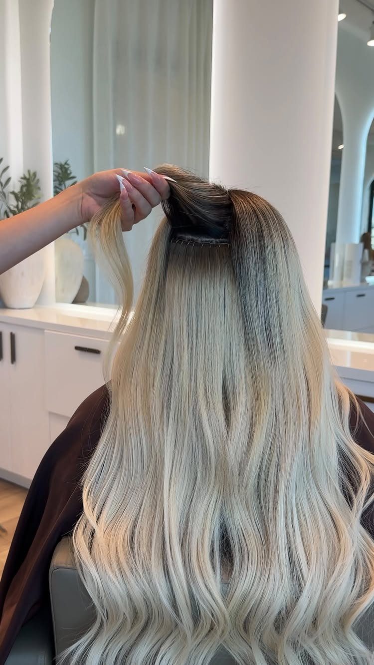 Long platinum blonde extensions add length and volume to dark-rooted hair in a salon