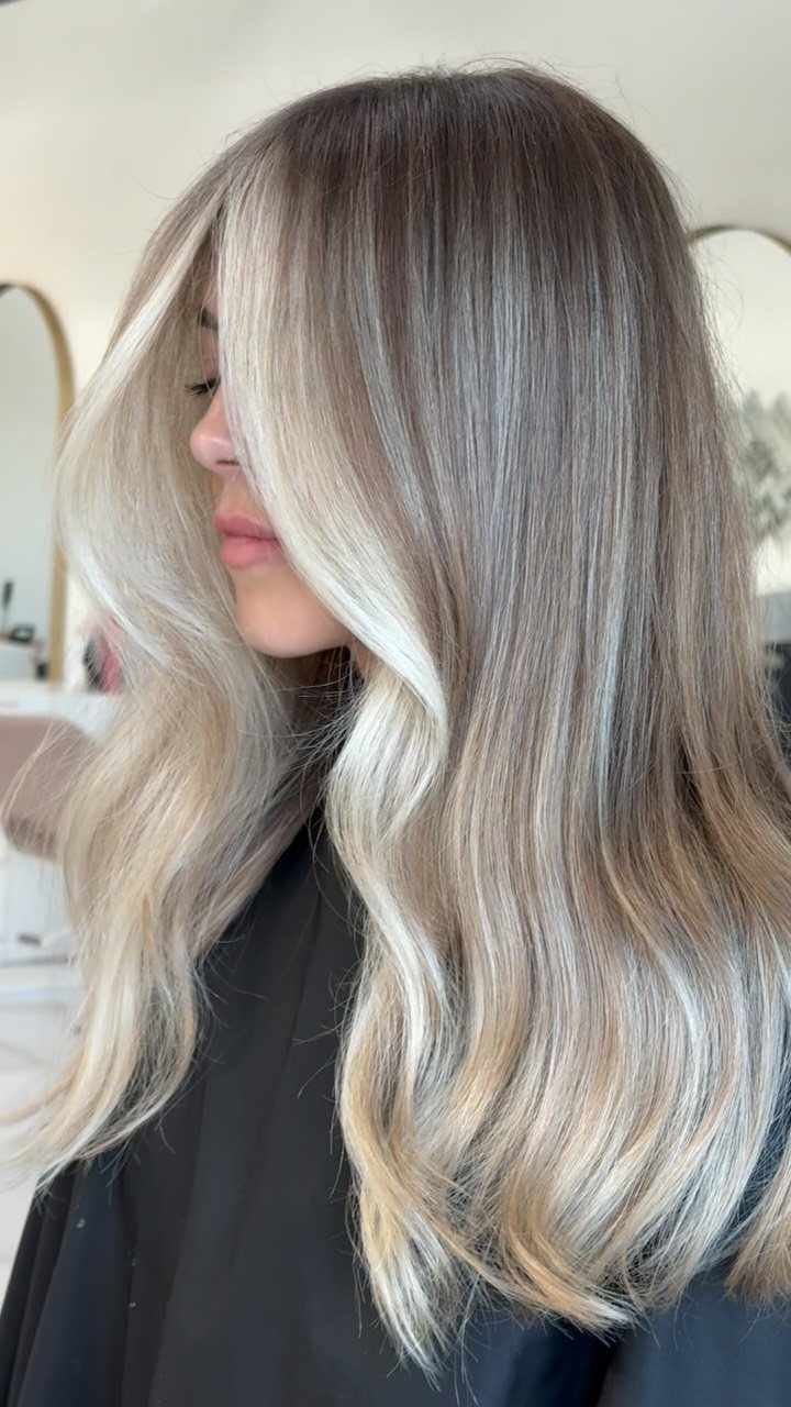 Woman showing long wavy hair with blended icy blonde balayage and dark roots