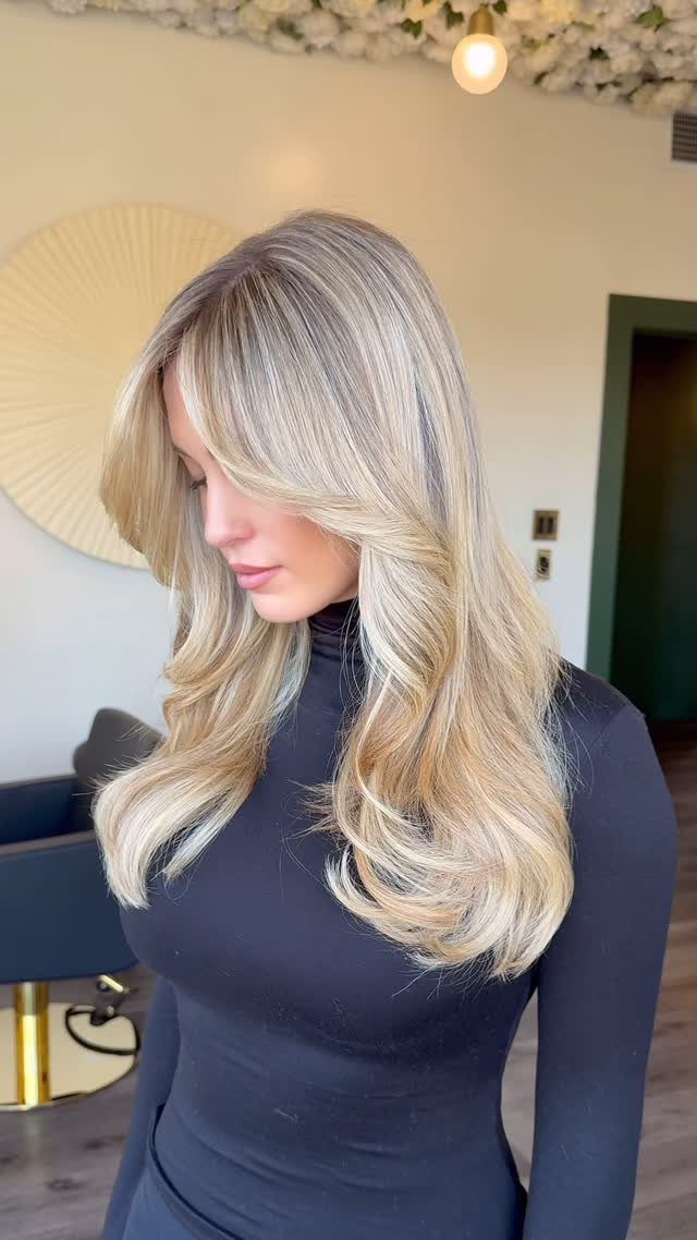 Long icy blonde highlighted waves with darker roots on a woman in a salon