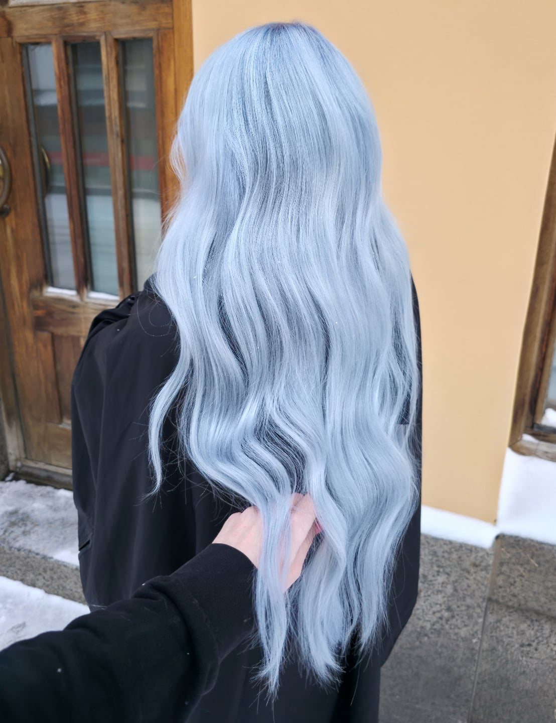 Long wavy icy blue-blonde hair falls down the back of a person