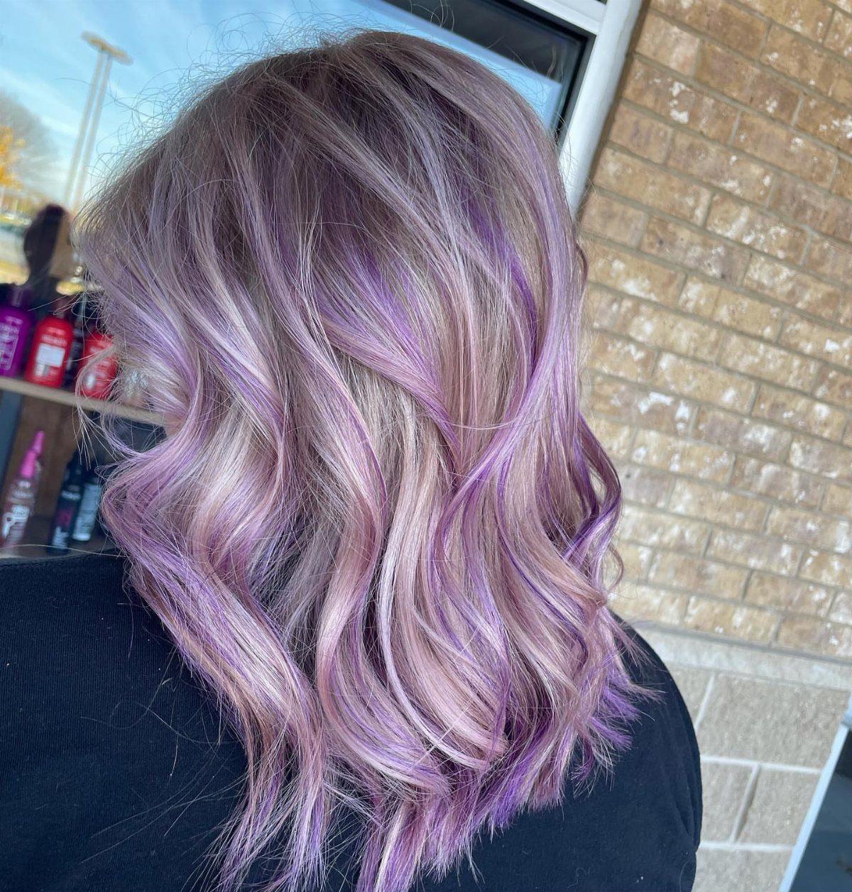 Silver and lavender-purple curls fall over a dark top in a salon