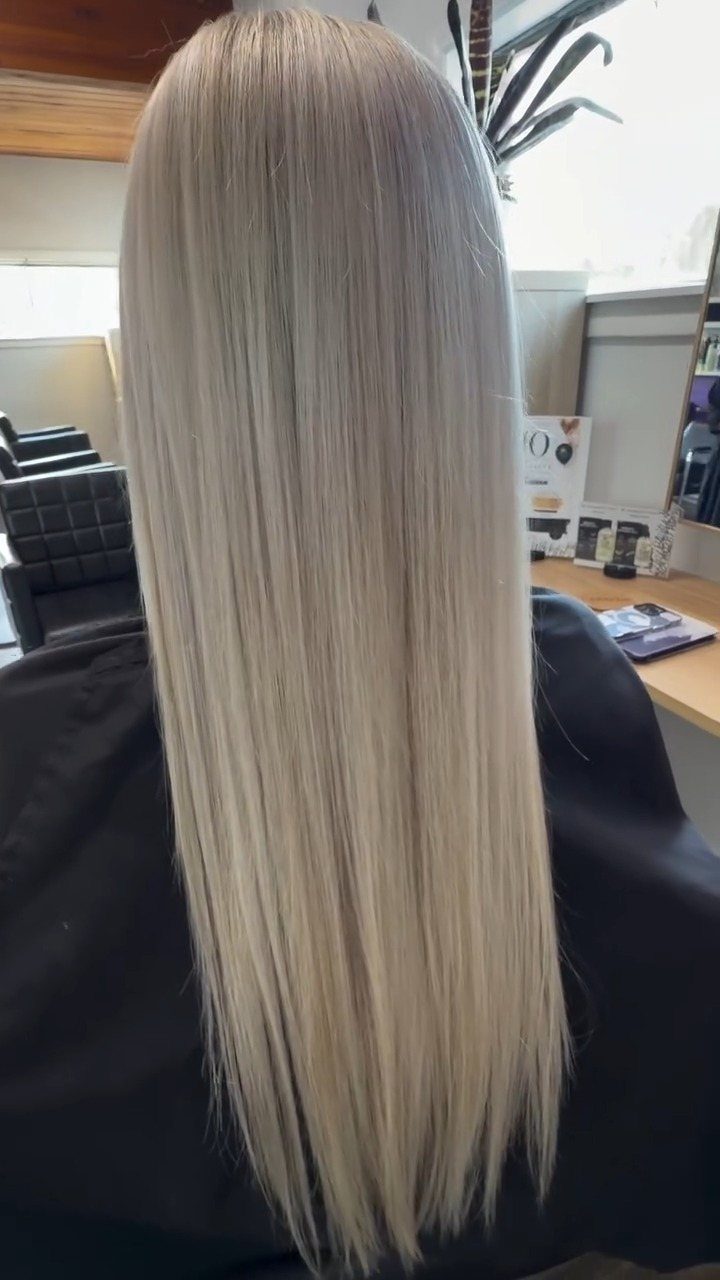 Long straight light ash blonde hair with subtle darker roots in a salon