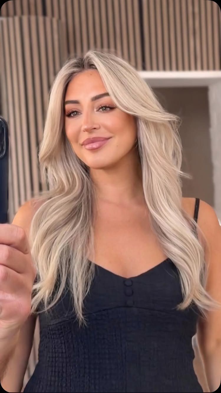 Woman with long, center-parted pearly blonde waves wearing a black sleeveless top