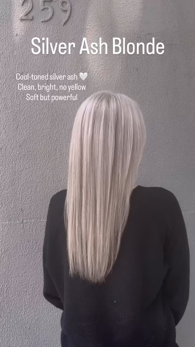 Long straight silver-blonde hair falls down the back of a person wearing black