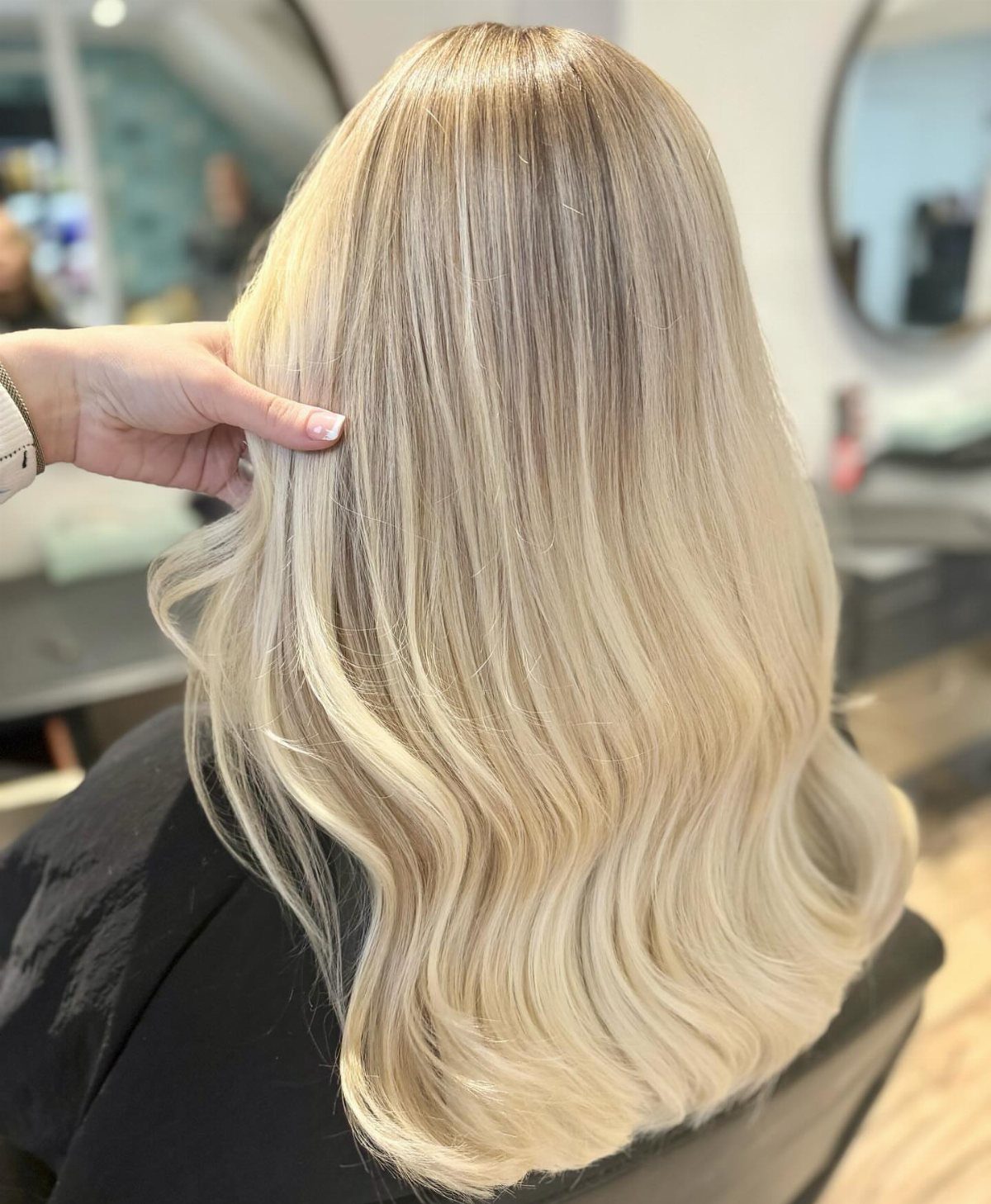 Long biscuit blonde hair with darker roots and softly waved ends in a salon