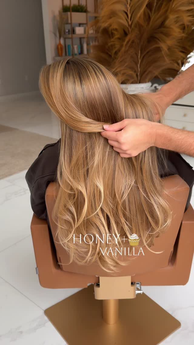 Long honey-blonde waves being styled in a salon chair with visible darker roots