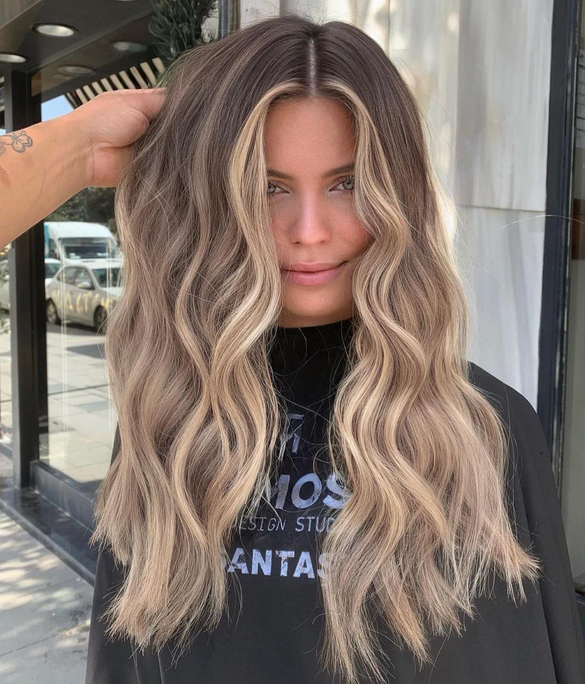 Woman with long wavy beige-blonde hair and darker roots in a salon cape