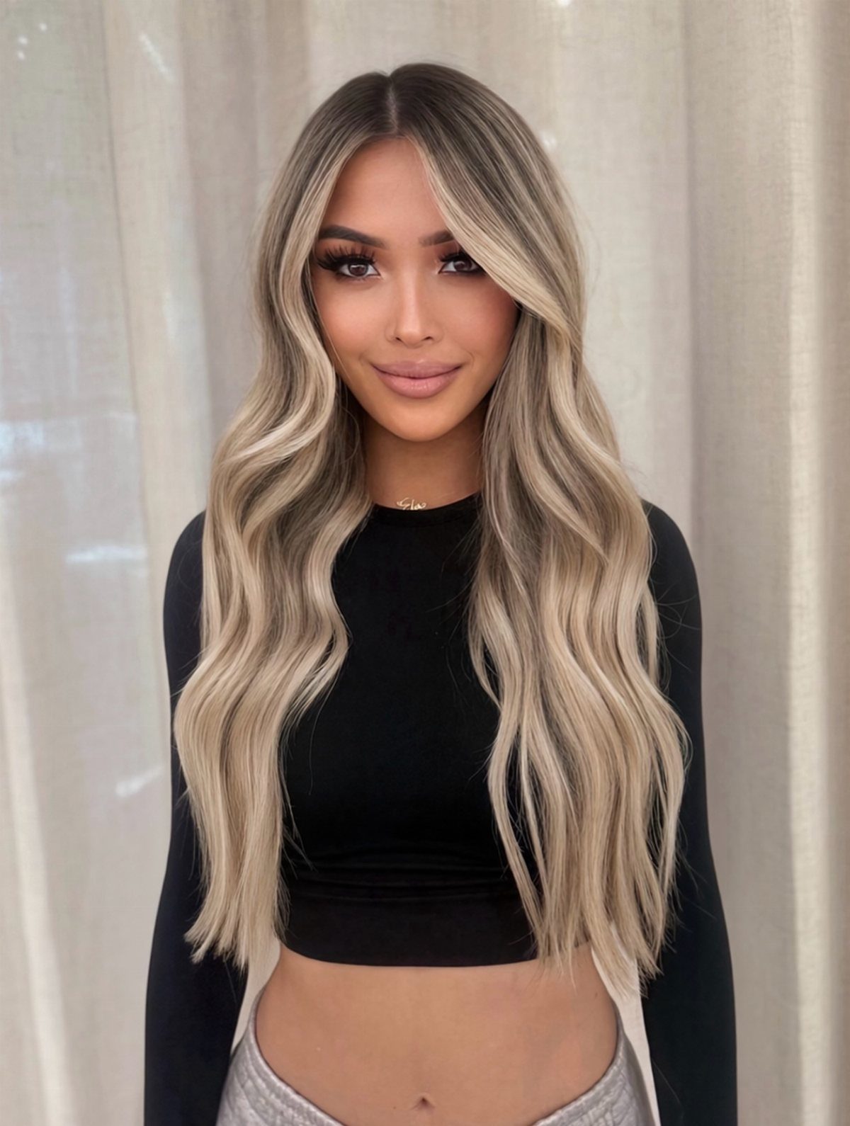Woman with long wavy blonde hair, dark roots, and bright face-framing highlights