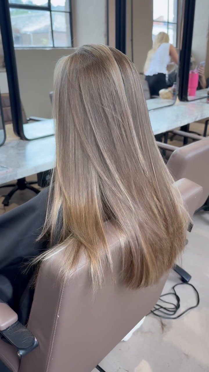 Long light brown hair with subtle blonde highlights in a salon chair