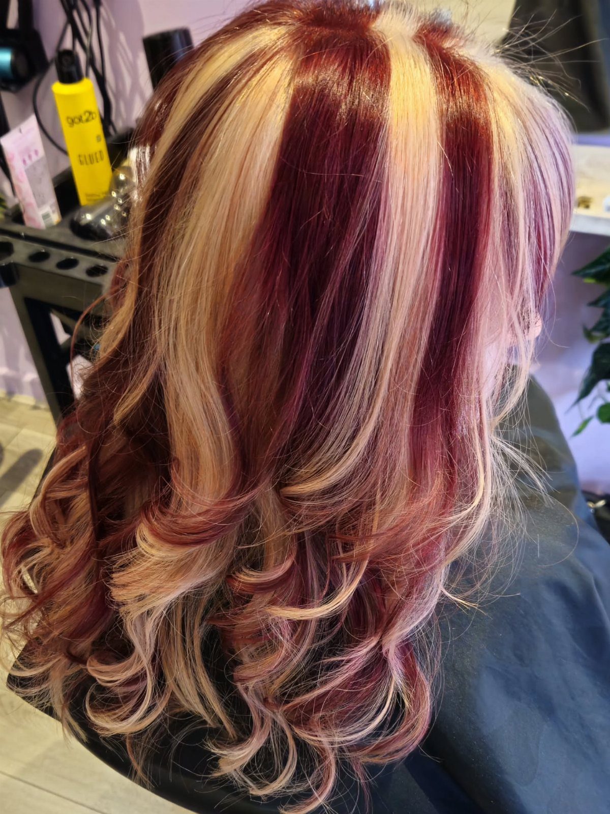 Layered blonde hair with burgundy-red streaks curled at the ends
