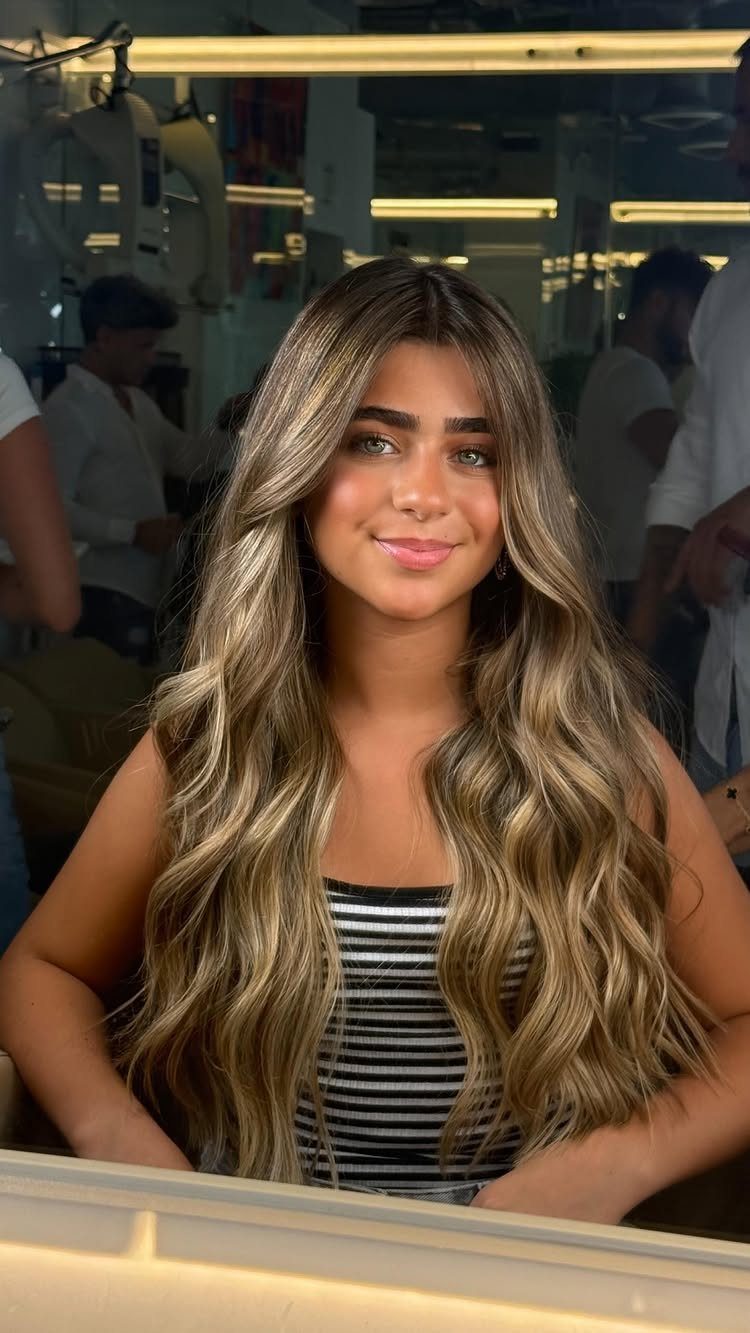 Young woman showing long wavy dirty blonde hair with lighter highlighted strands