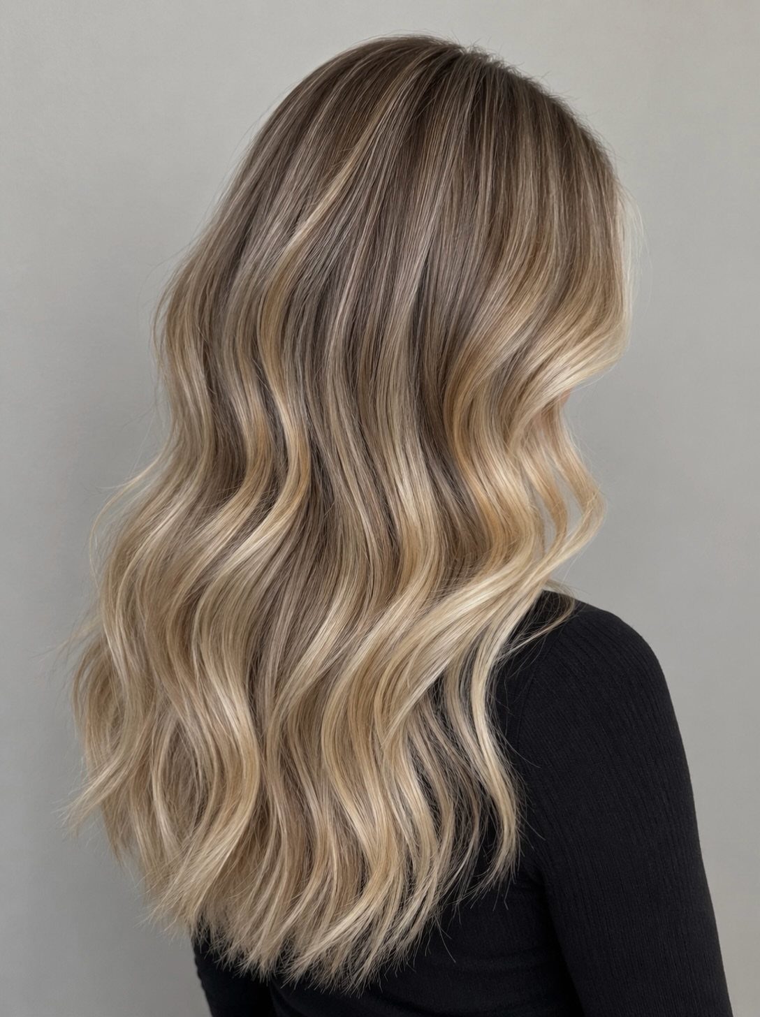 Wavy dark blonde hair gradually transitions from darker roots to bright beige-blonde ends