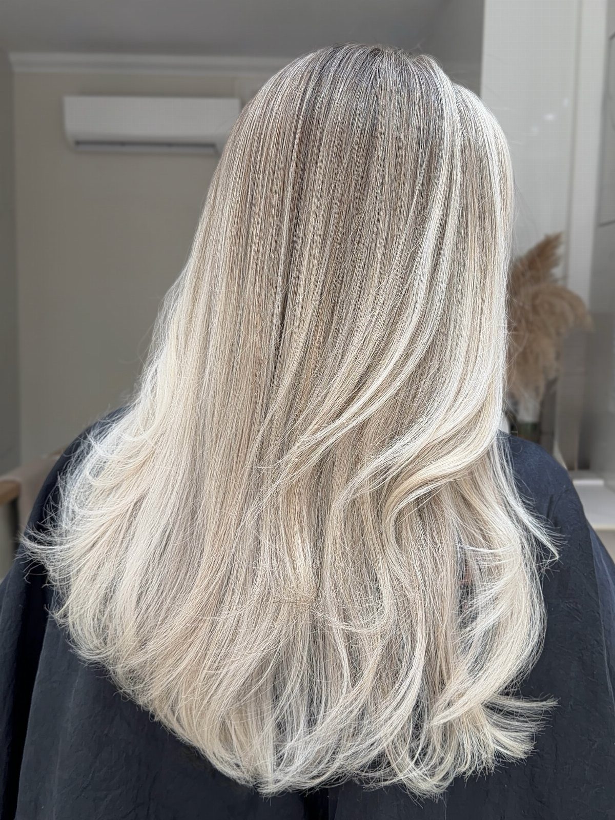 Long layered platinum blonde hair with darker roots shown from behind