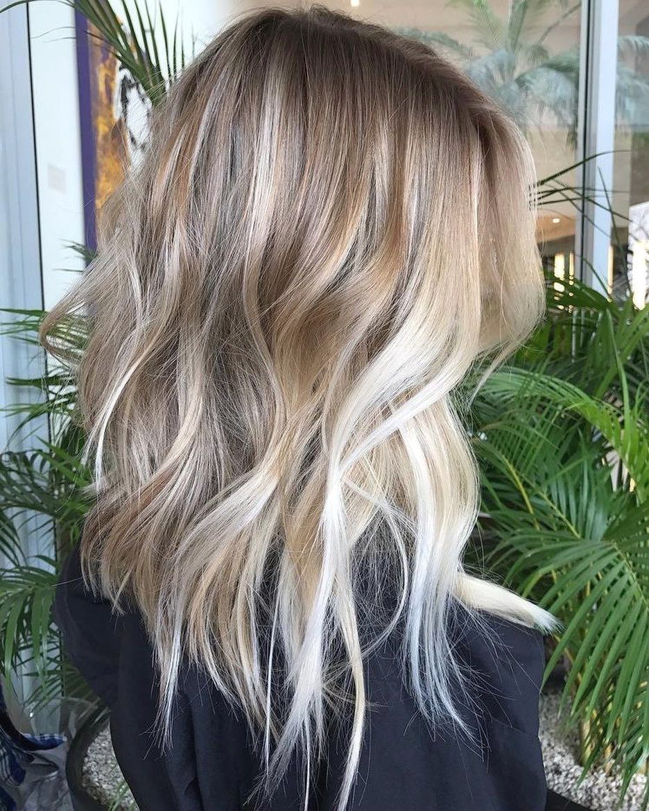 Long wavy blonde hair with dark roots and blended beige and pale strands