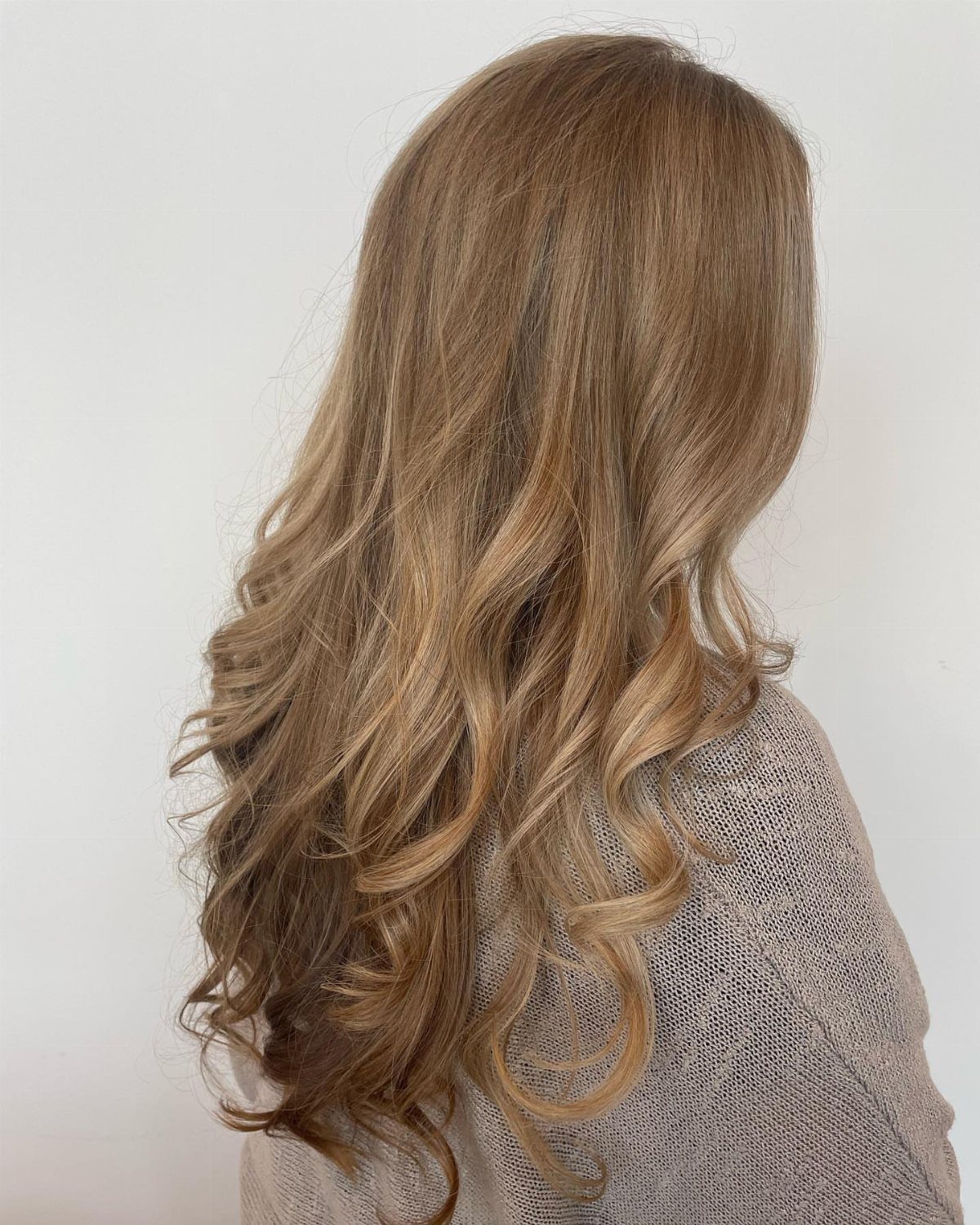 Long curled wheat-blonde hair with warm highlights against a light background