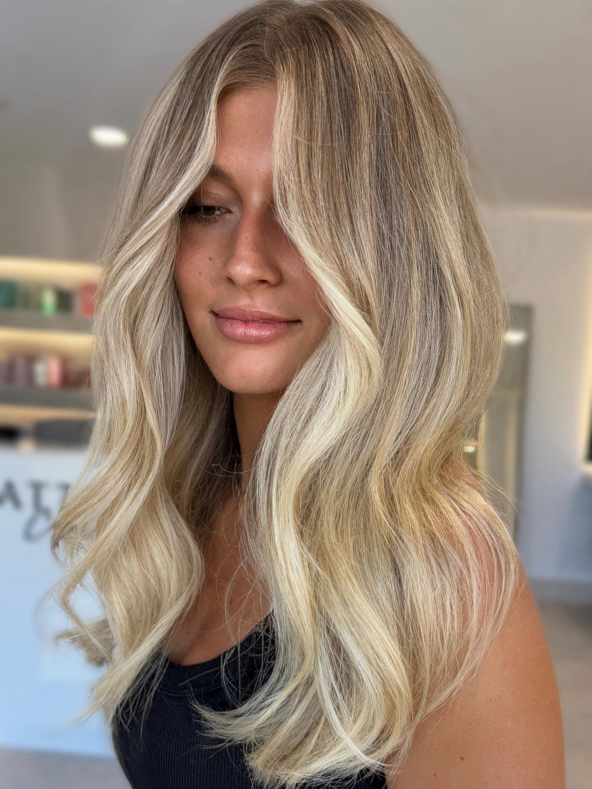 Woman displaying long dimensional blonde hair with darker roots and creamy waves