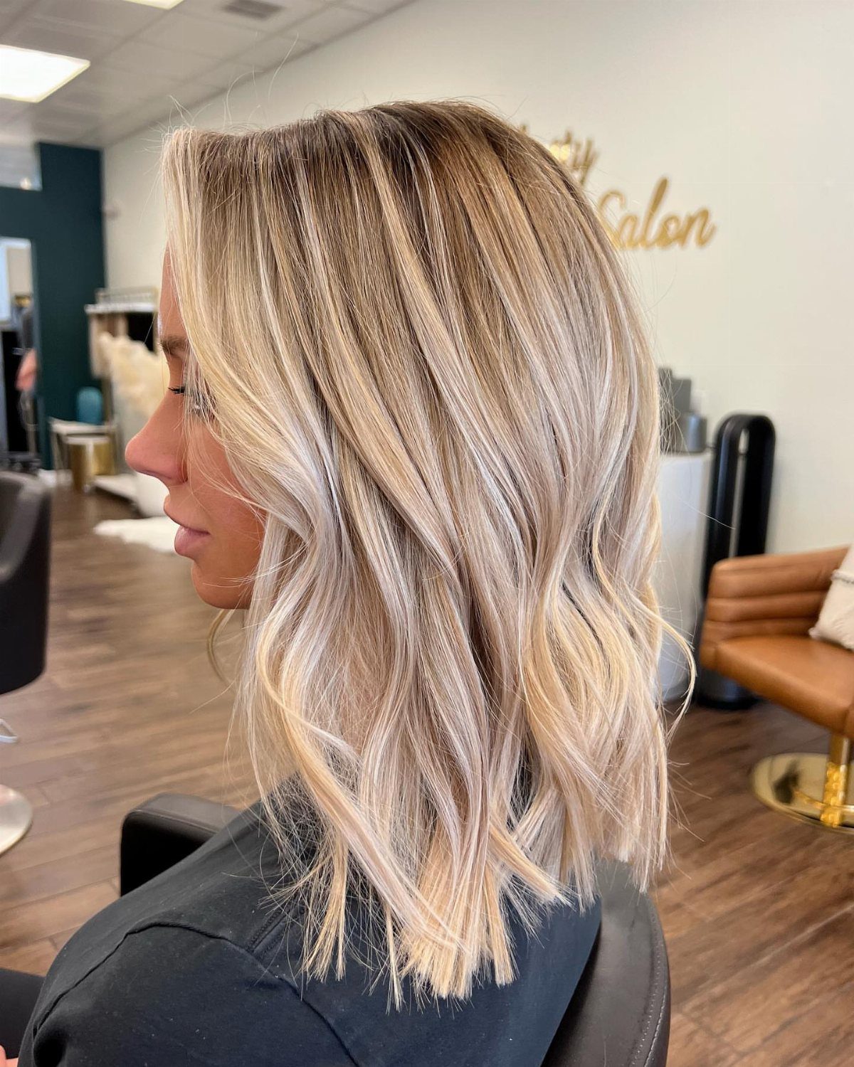 Shoulder-length blonde hair with staggered highlights and darker roots in a salon