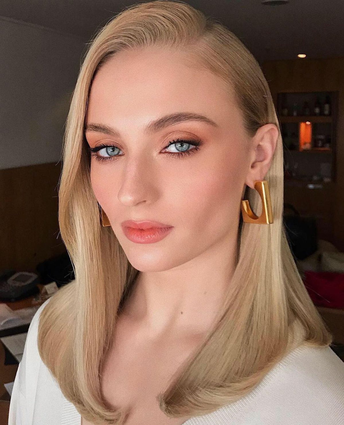 Woman with shoulder-length honey-blonde hair and gold earrings poses indoors