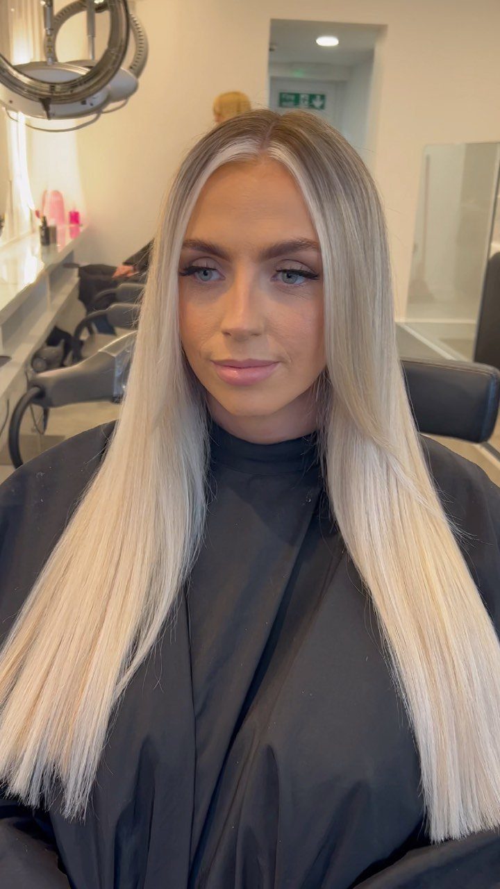 Woman with long straight platinum blonde hair and darker roots in a salon chair