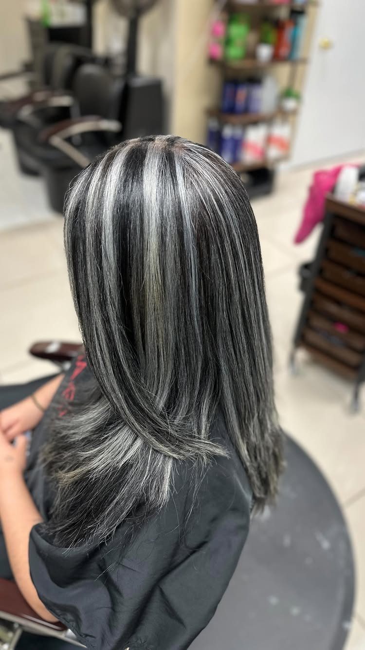 Dark layered hair with bright platinum highlights sits in a salon chair.