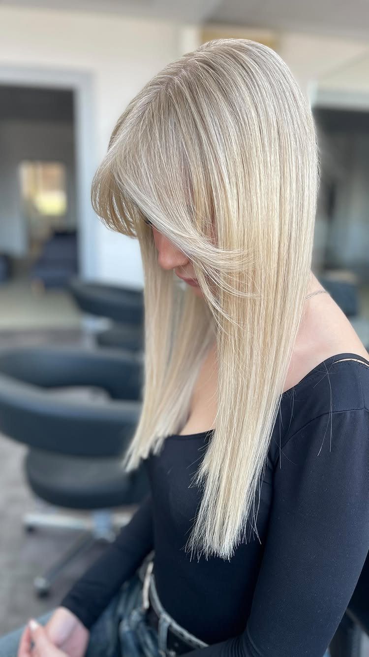 Long straight pale blonde hair with layered side-swept bangs in a salon