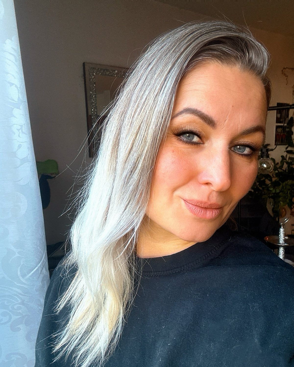 Woman with long, side-parted platinum blonde hair posing indoors