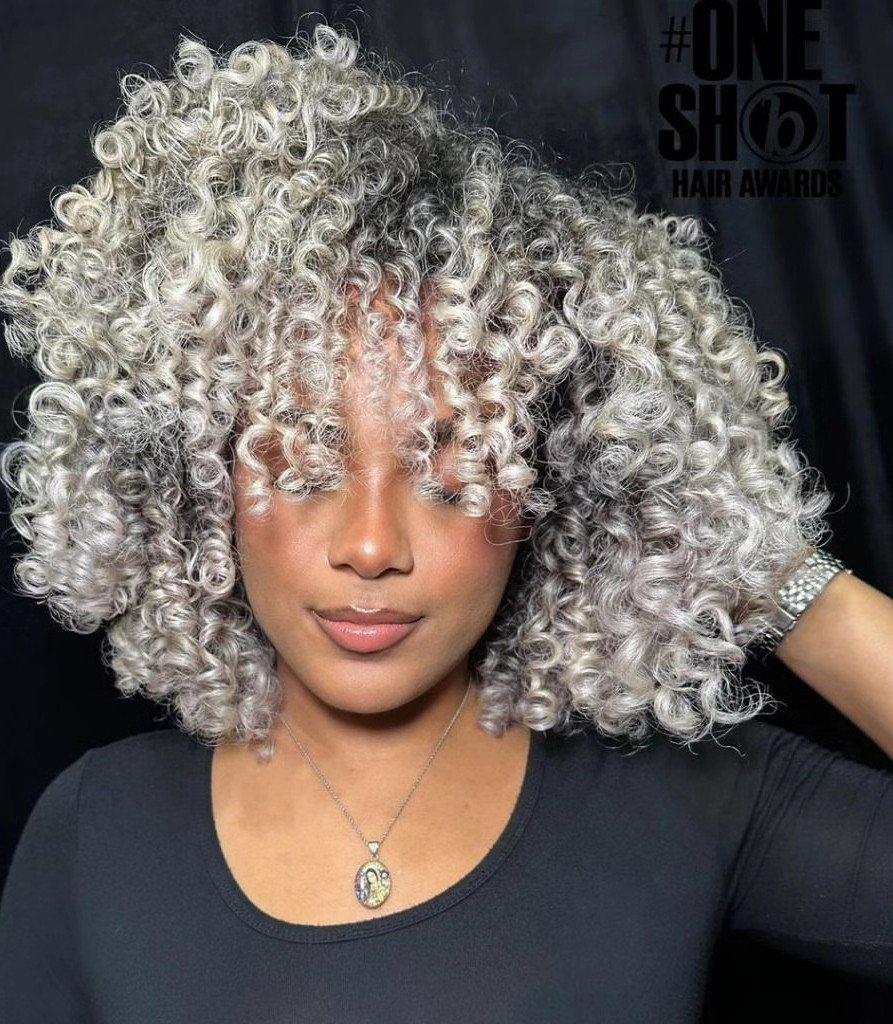 Voluminous platinum curls frame a person wearing a black top and pendant