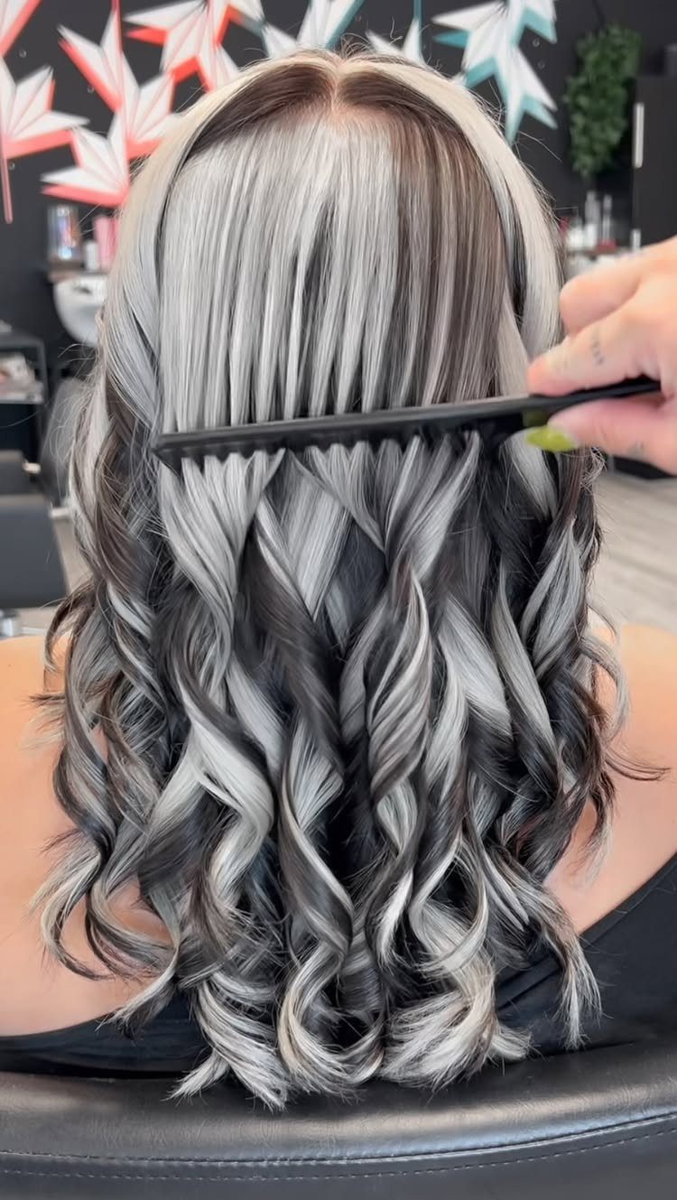 Platinum curls with dark brown lowlights being combed in a salon