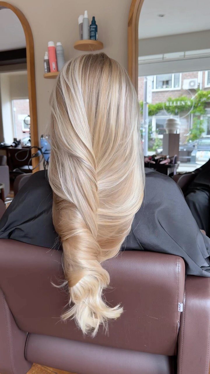Platinum blonde hair styled in flowing layers and a loose low twist in a salon