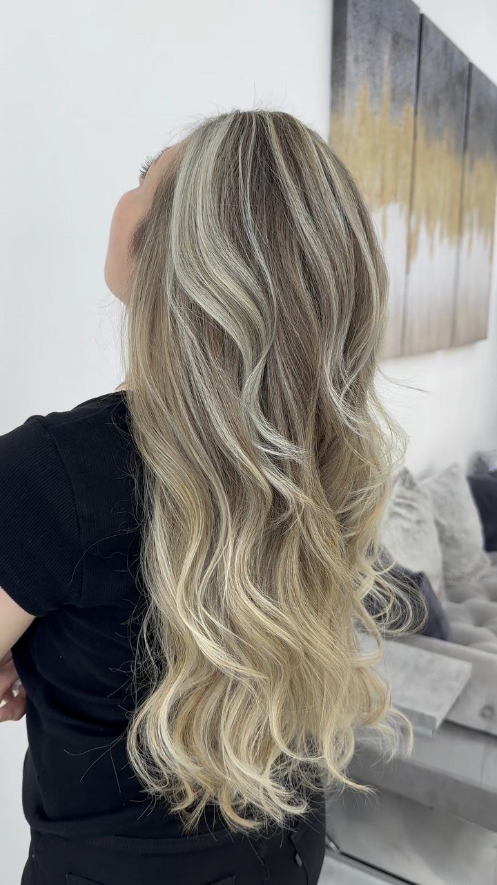 Long wavy platinum blonde hair with blended darker roots cascading over a black top