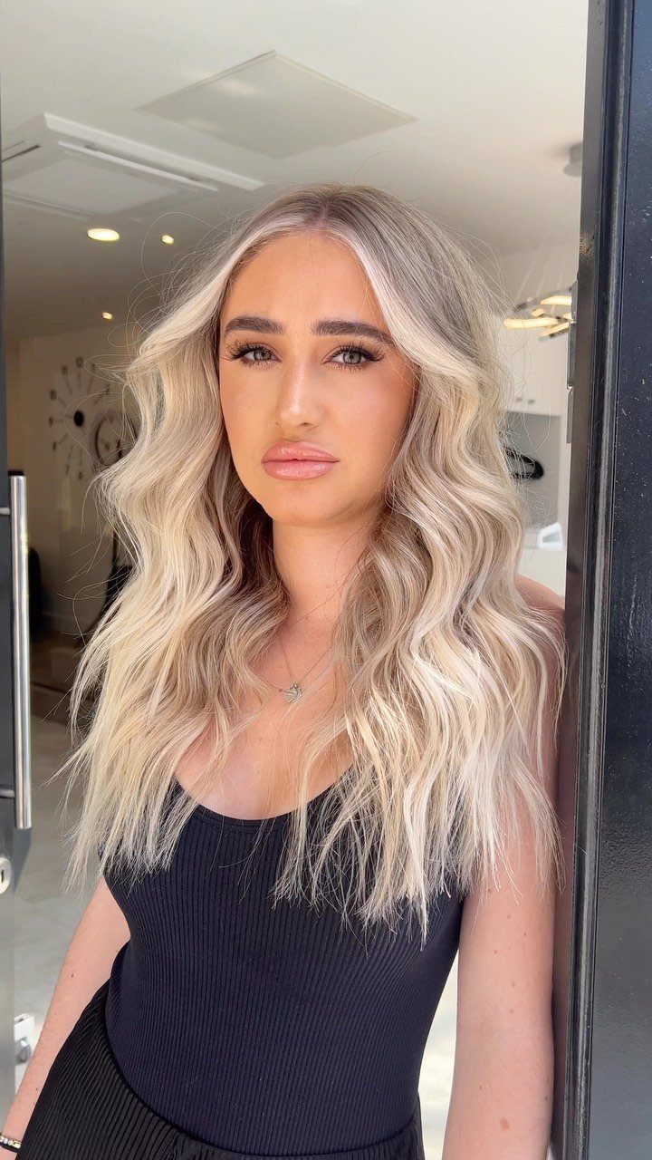 Woman with long, softly wavy vanilla platinum blonde hair and darker roots