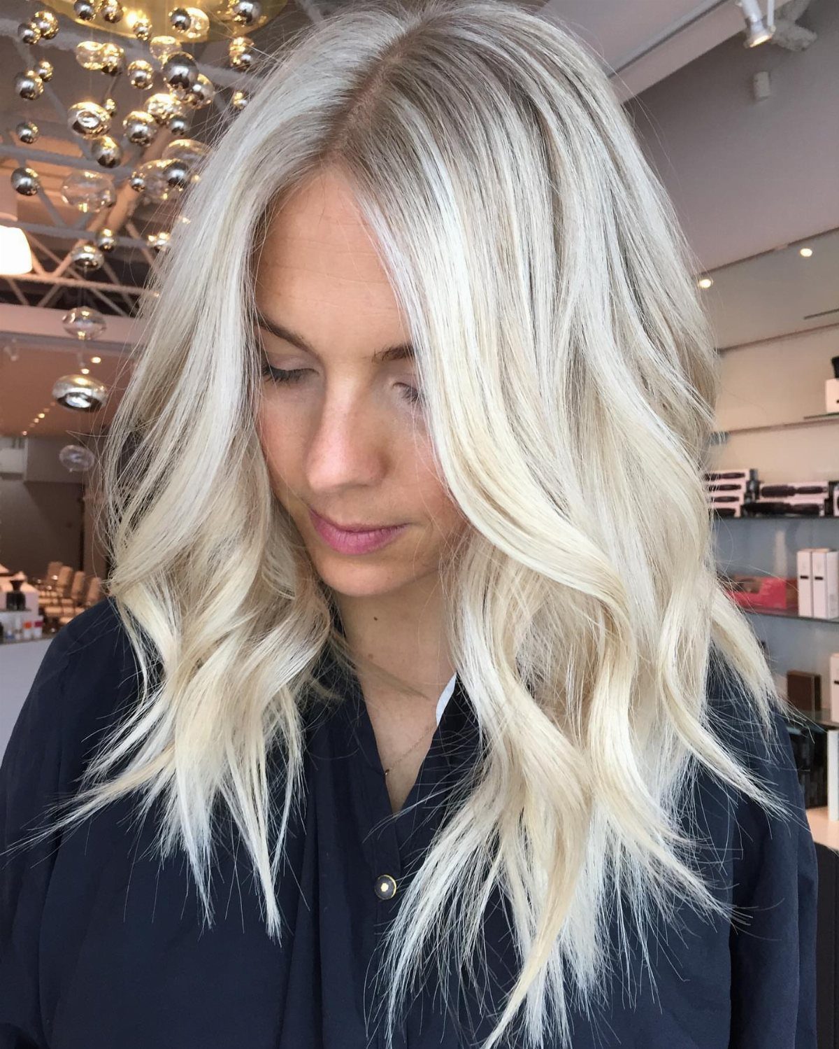 Woman with long, wavy platinum blonde hair and darker roots in a salon