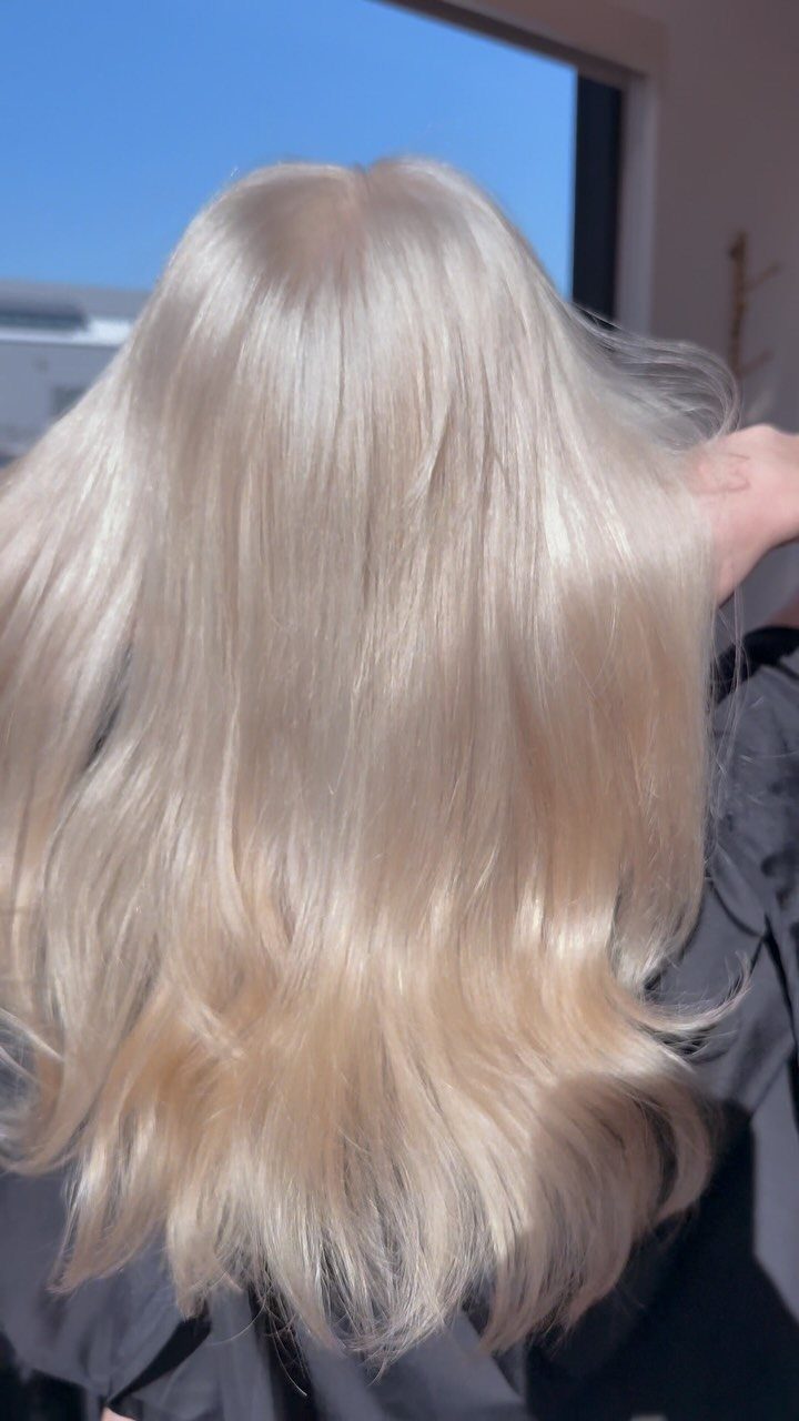Long, wavy platinum blonde hair shown from behind near a window