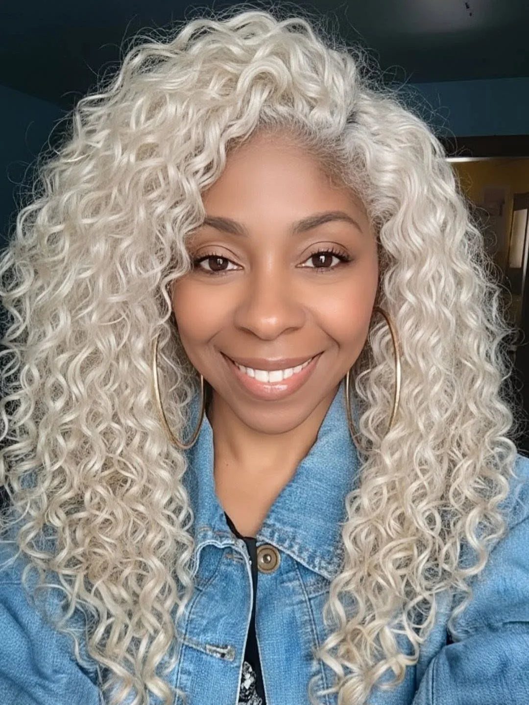 Woman with long, defined platinum blonde curls wearing a blue denim jacket
