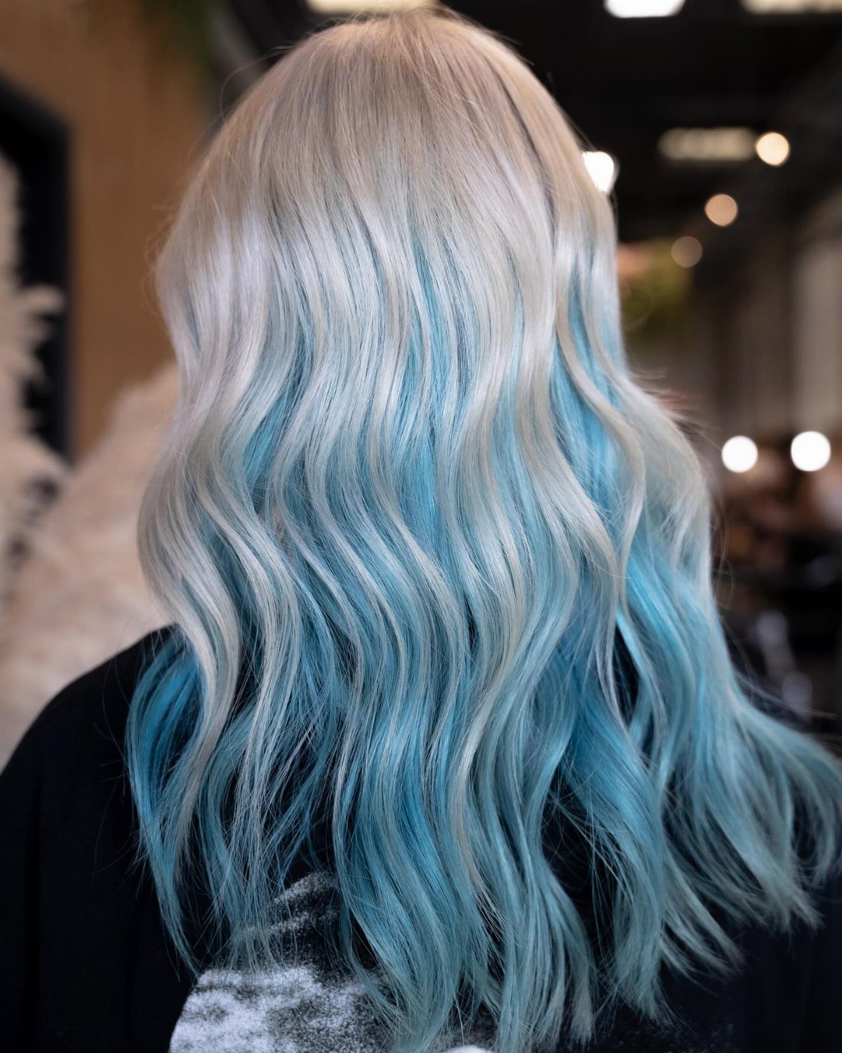 Long wavy platinum hair with icy silver-blue tones over a black top