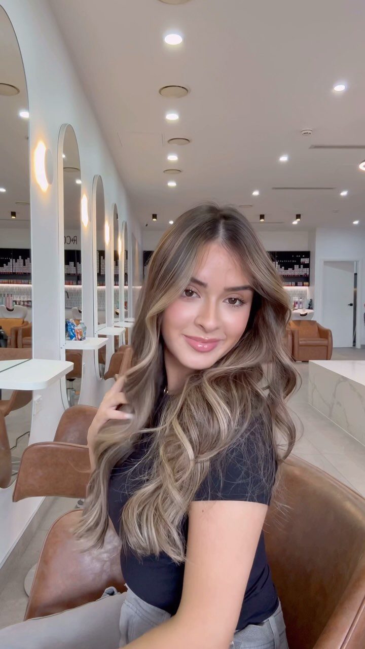 Woman displaying long wavy bronzed sandy blonde hair in a modern salon