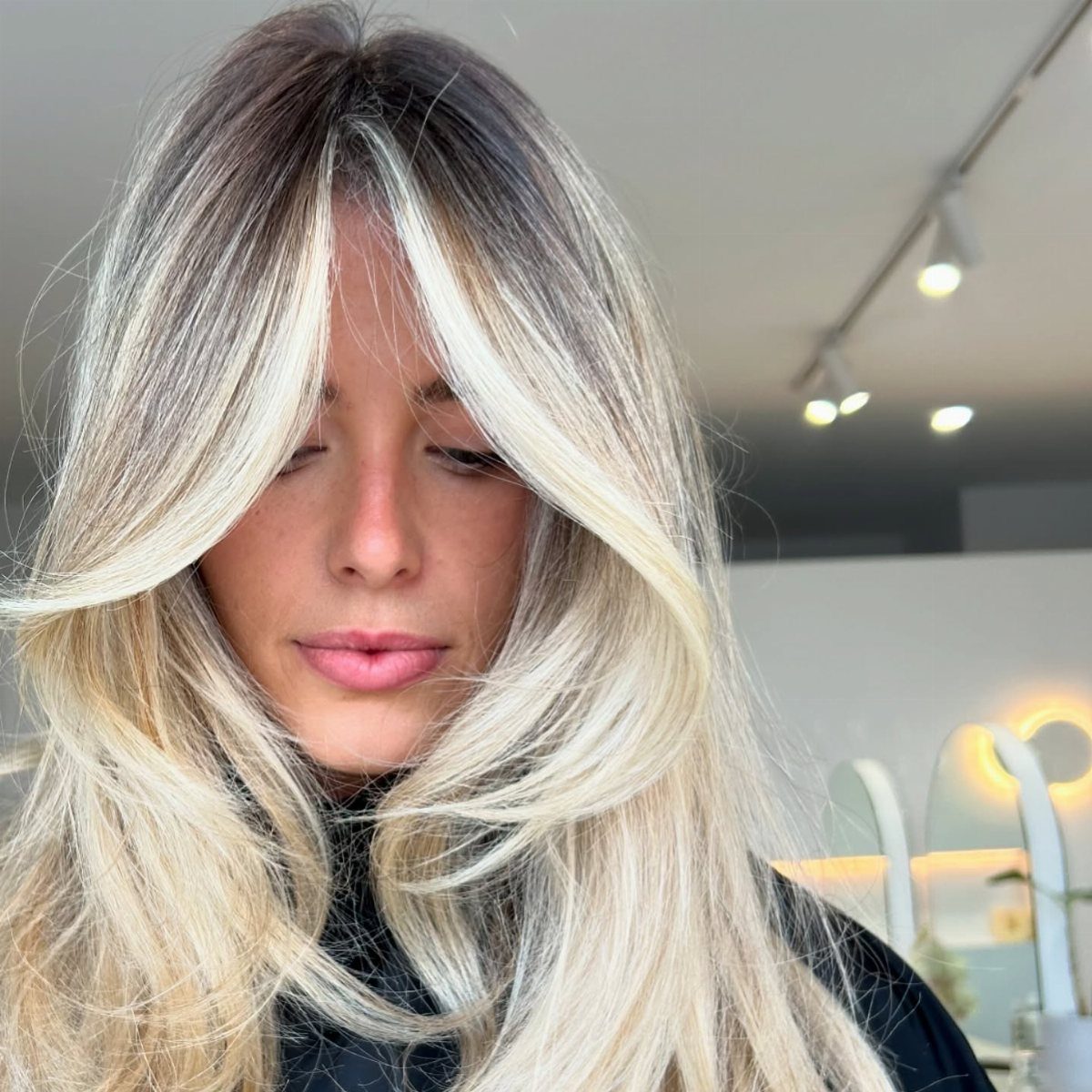 Long blonde hair with pale sandy face-framing pieces and dark roots