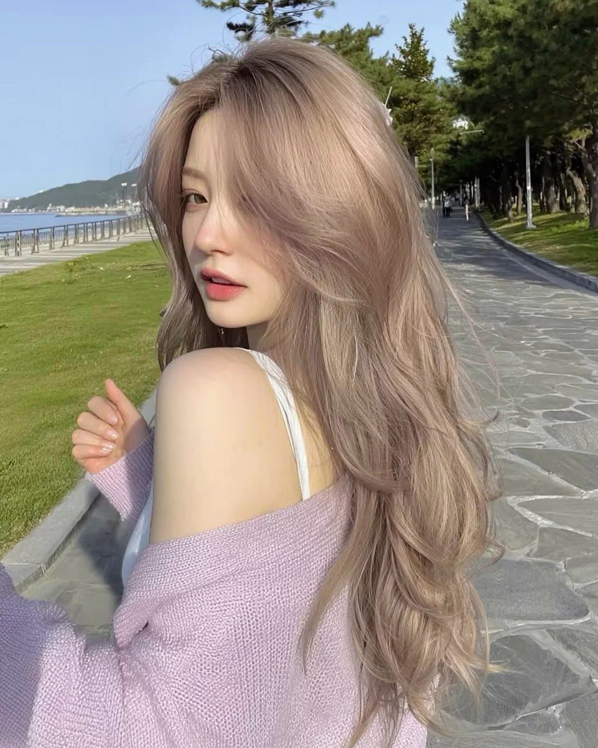 Woman showing long, airy light sandy blonde waves beside a seaside path