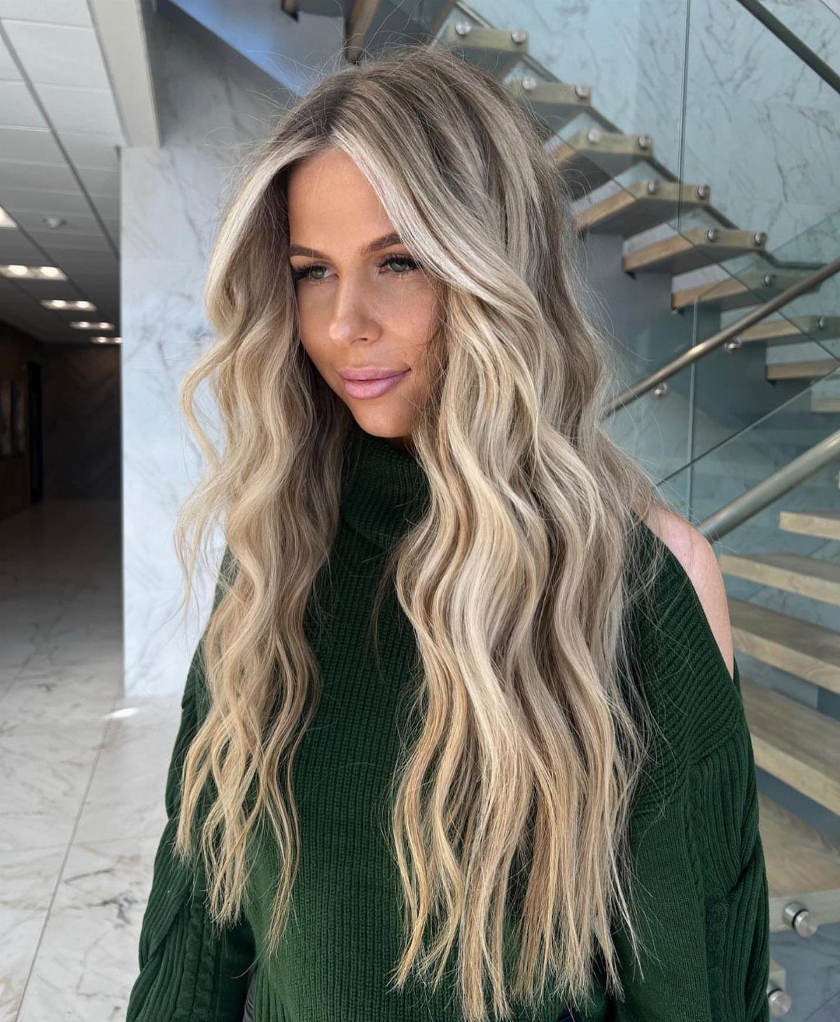 Woman with long wavy sandy blonde hair and darker roots