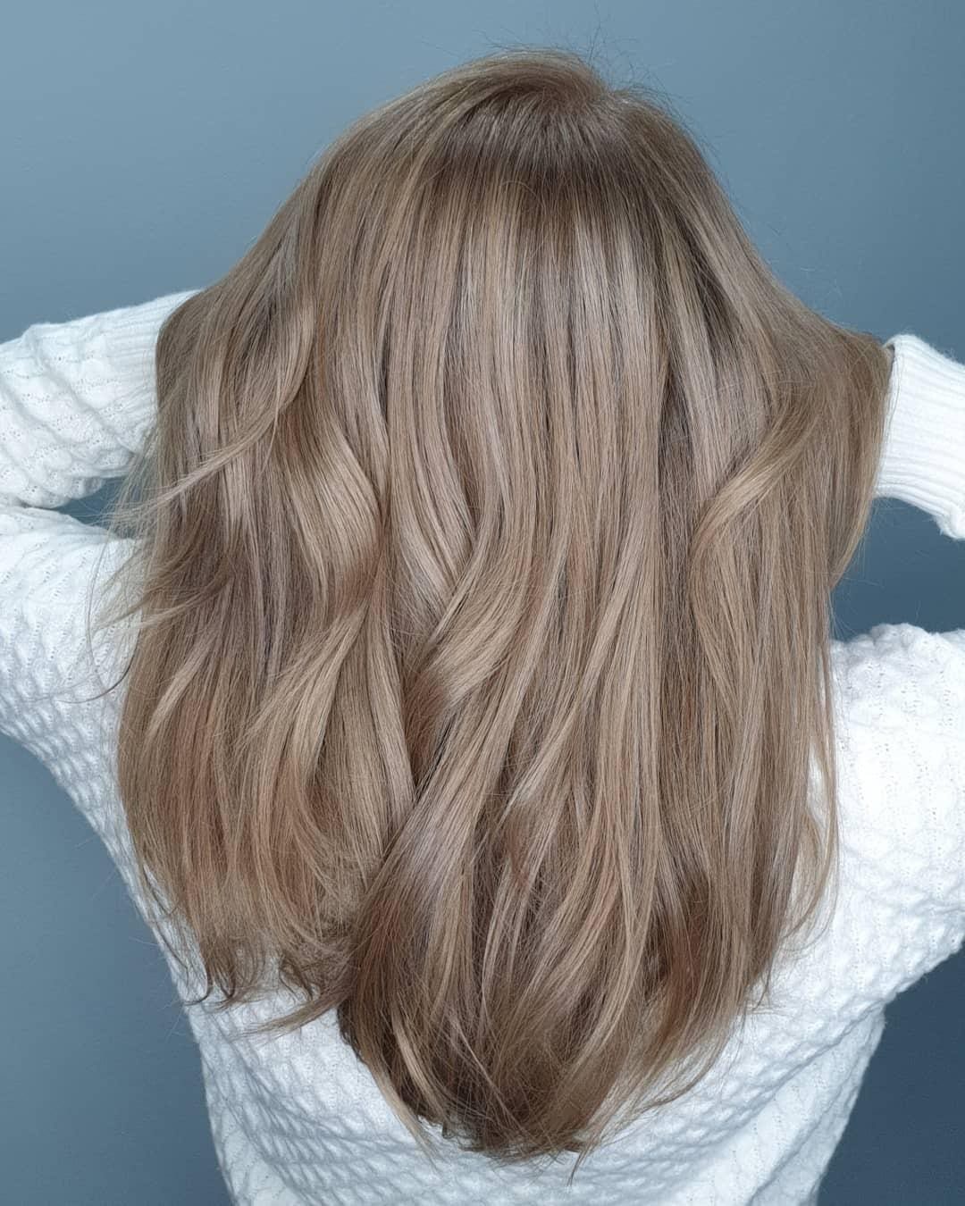 Layered beige-blonde hair shows cool, muted taupe tones and soft waves.
