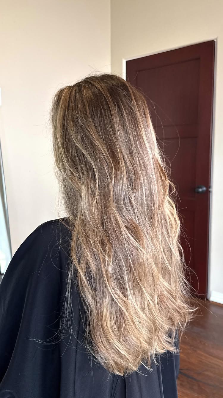 Long wavy hair shows blended brown and sandy blonde tones over a black cape