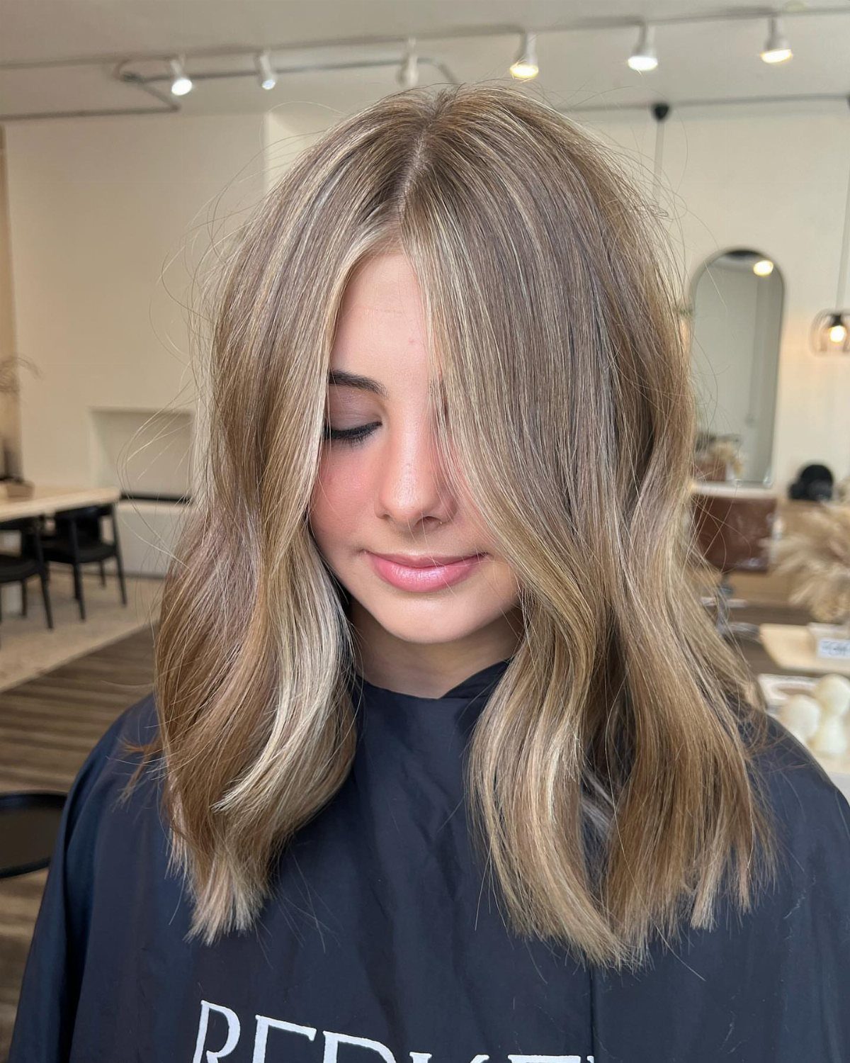 Woman showing softly waved sandy blonde hair with fine, subtle highlights in a salon