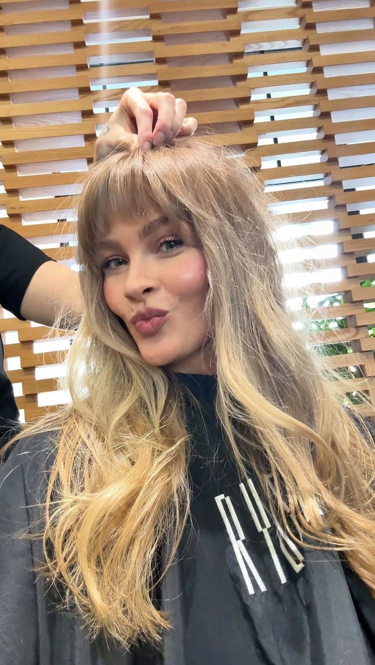 Woman posing with long sandy blonde waves and a wispy fringe