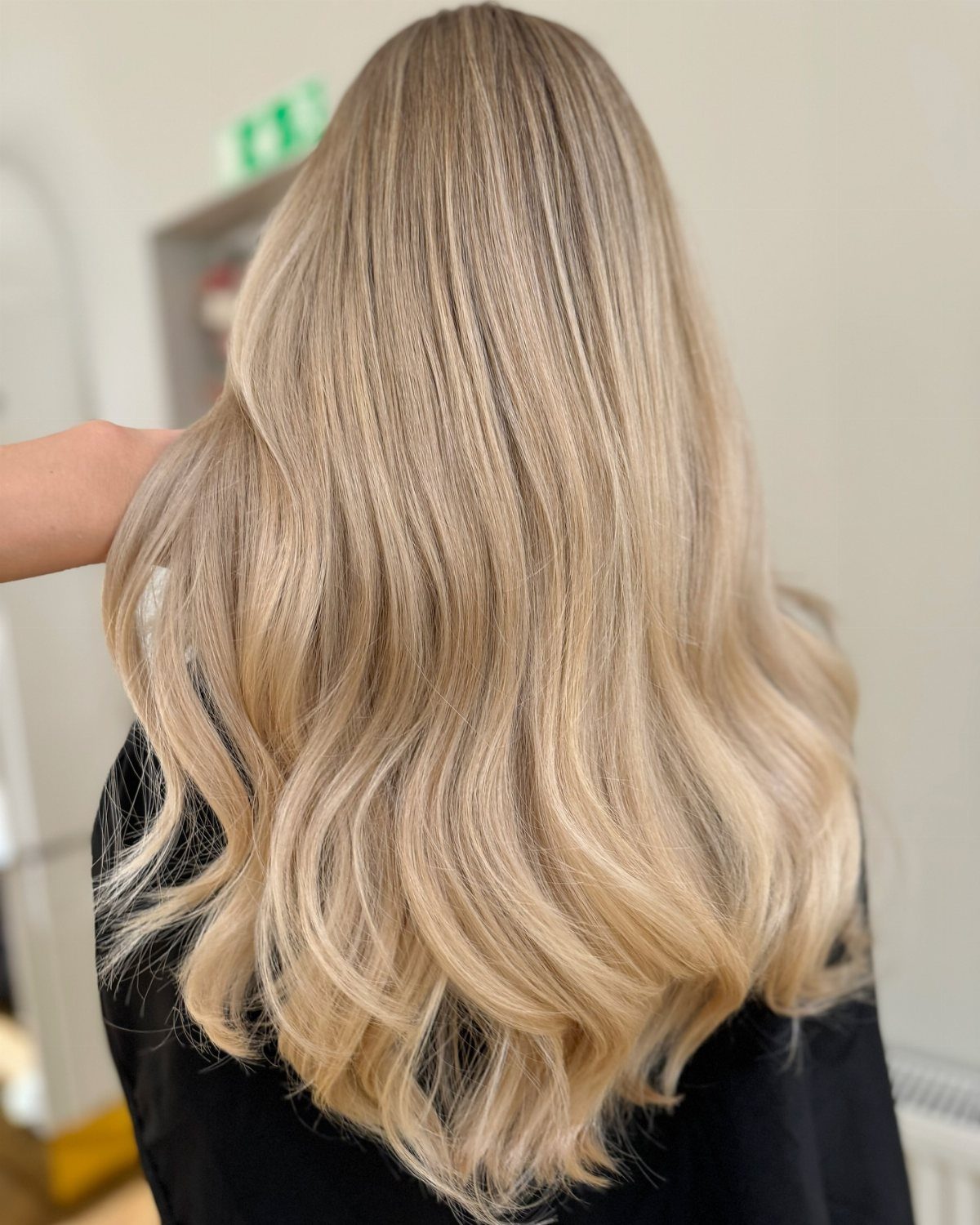 Long wavy blonde hair blends sandy beige roots with pale golden champagne tones