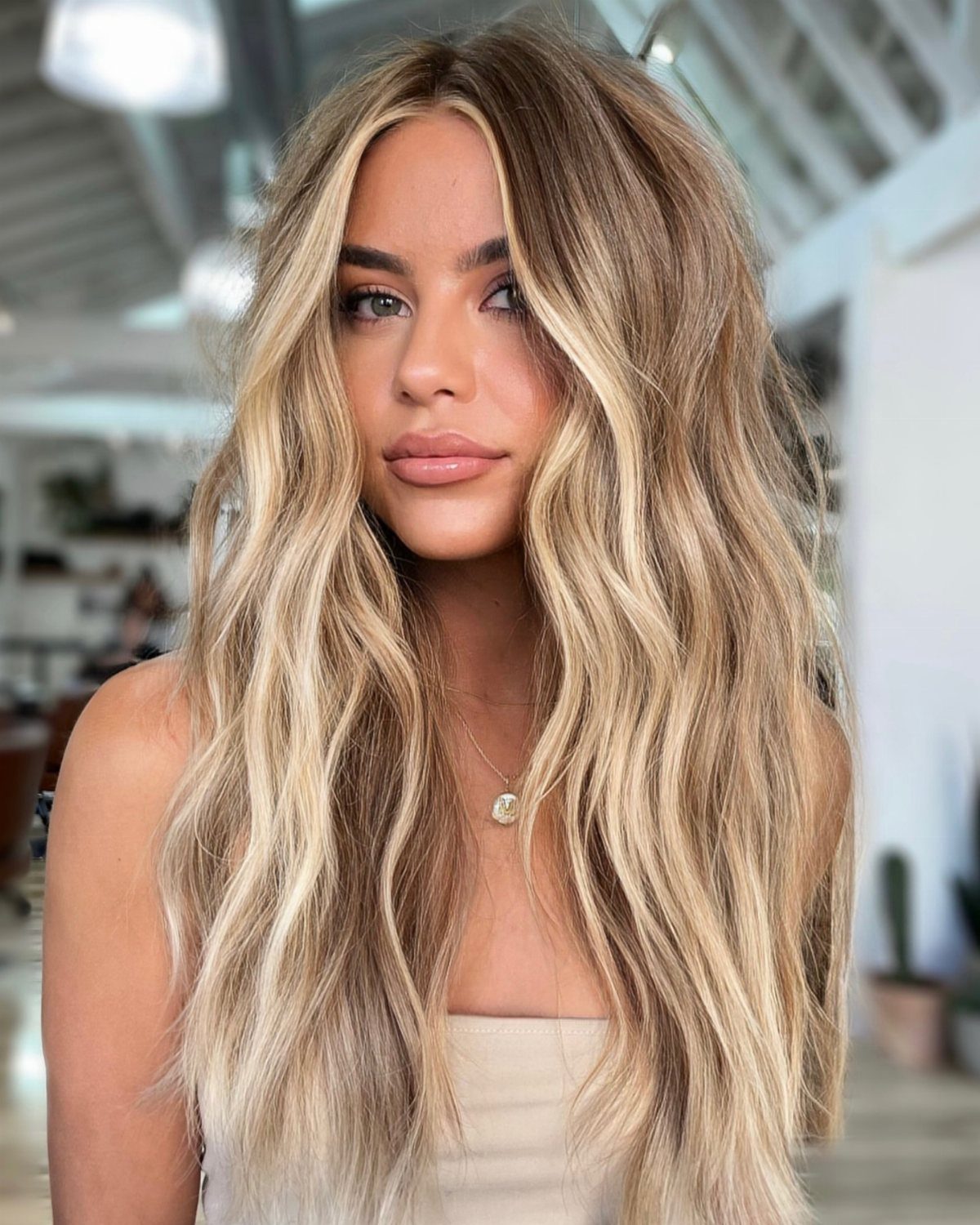 Woman with long wavy sandy blonde hair and darker roots posing indoors