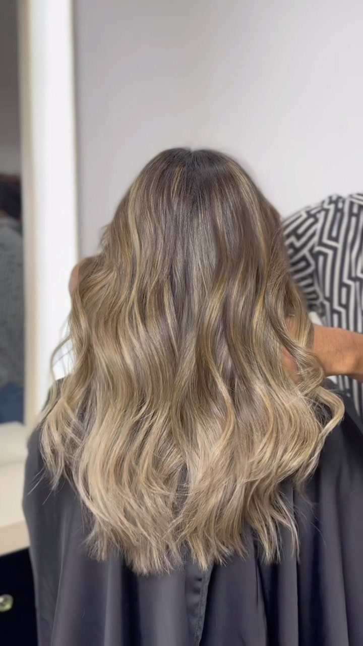 Long cool sandy blonde waves with darker roots over a dark salon cape